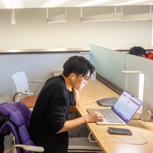 A student working on a laptop in a library. A student working on a laptop in a library.
