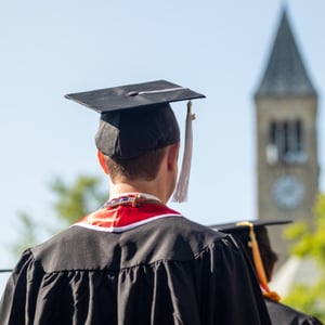 A man in a graduation cap and gown is looking at a clock tower.
